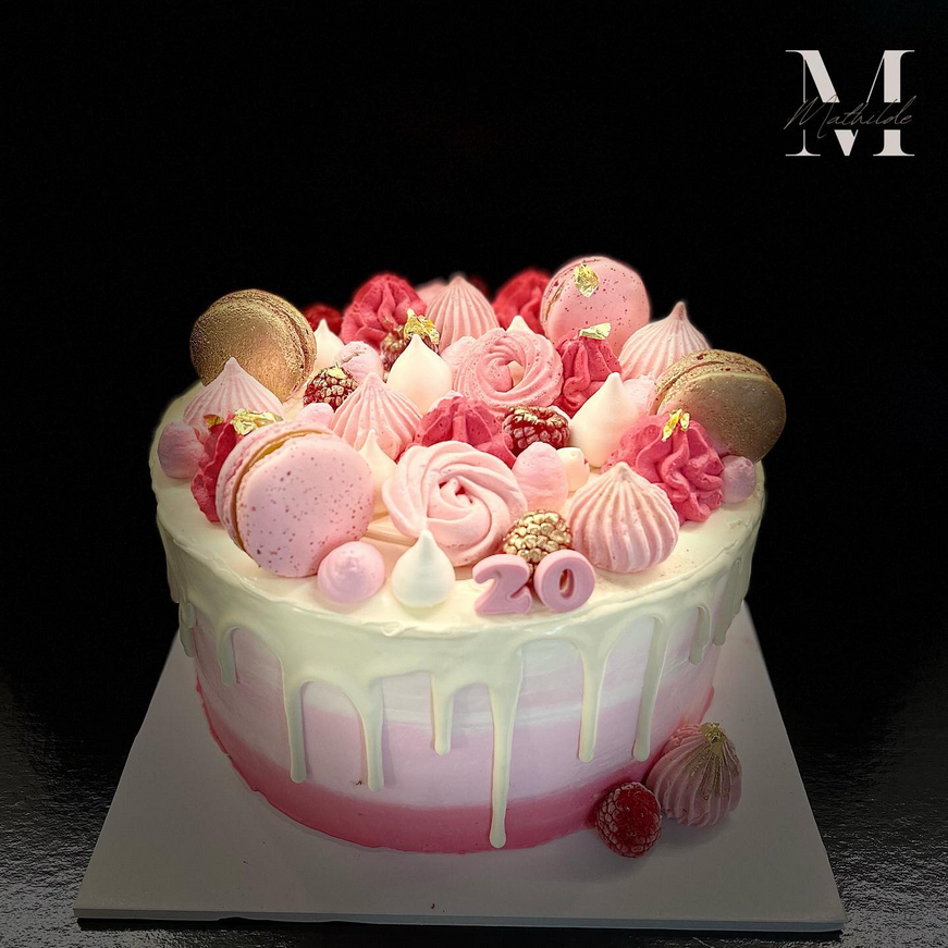 Un magnifique gâteau d'anniversaire rose et blanc, décoré de meringues roses, de macarons dorés et roses, et de fruits rouges, avec le chiffre "20".