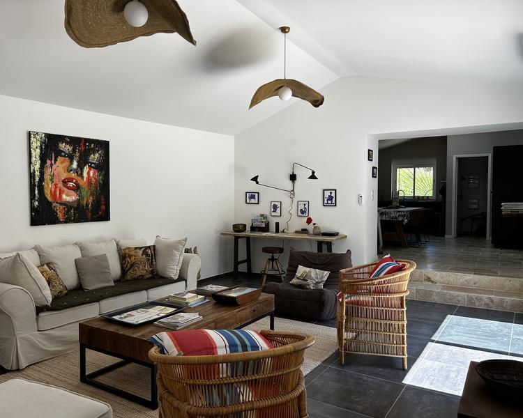 Un salon moderne avec un grand canapé blanc, une table basse en bois, et des chaises en rotin, décoré d'œuvres d'art et de luminaires originaux.