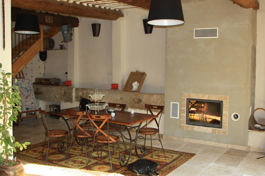 Une salle à manger rustique avec une table en bois, des chaises, une cheminée, des poutres apparentes au plafond et une plante verte en pot.