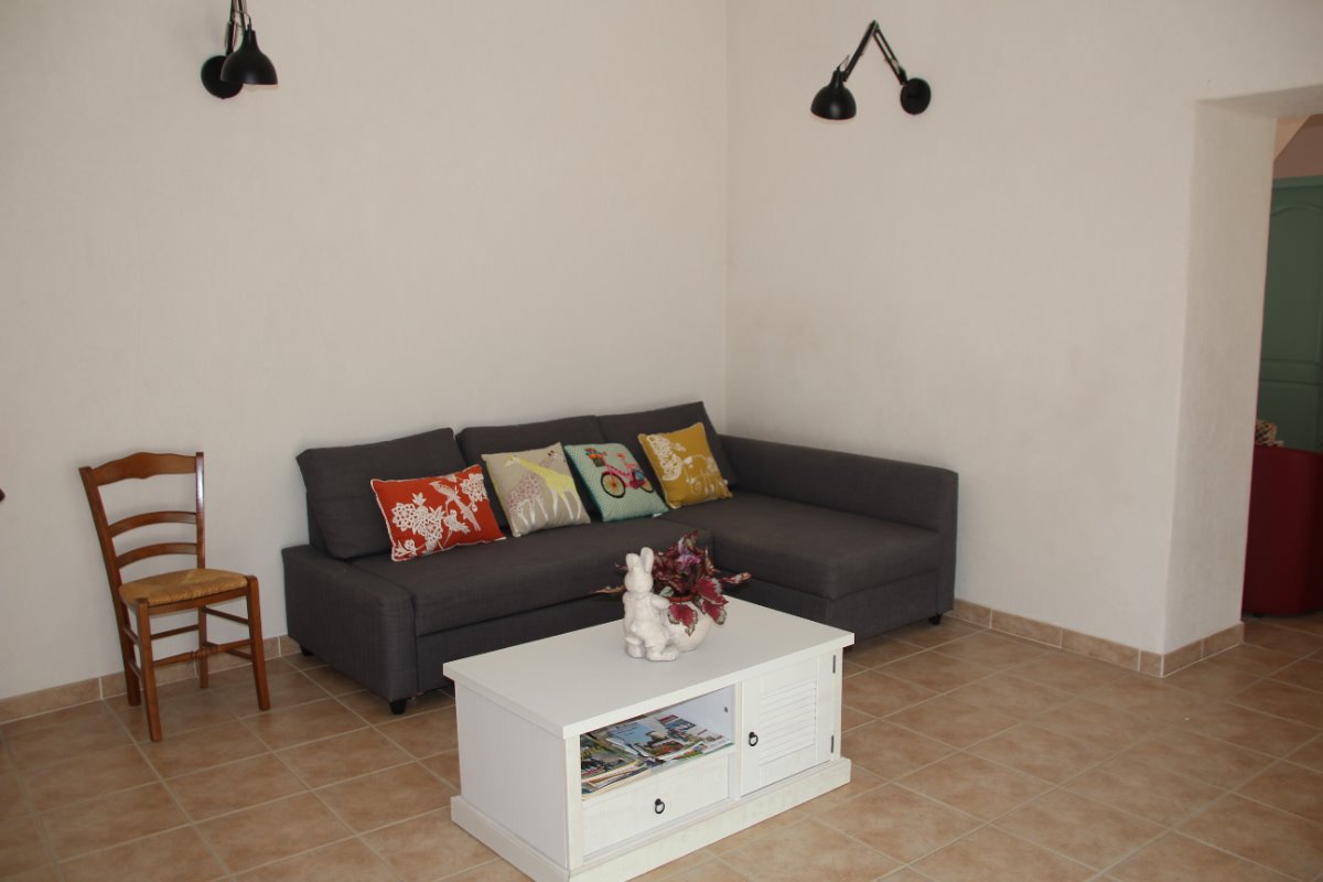 Un salon moderne avec un canapé gris orné de coussins colorés, une table basse blanche décorée, une chaise en bois et des appliques murales noires.
