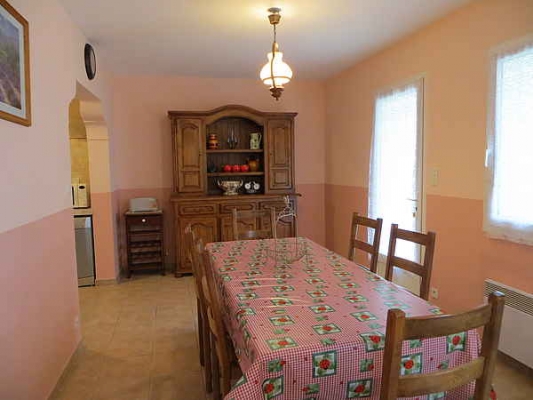 Une salle à manger chaleureuse avec une grande table recouverte d'une nappe à carreaux, des chaises en bois, une commode ancienne et un buffet rempli d'objets décoratifs.