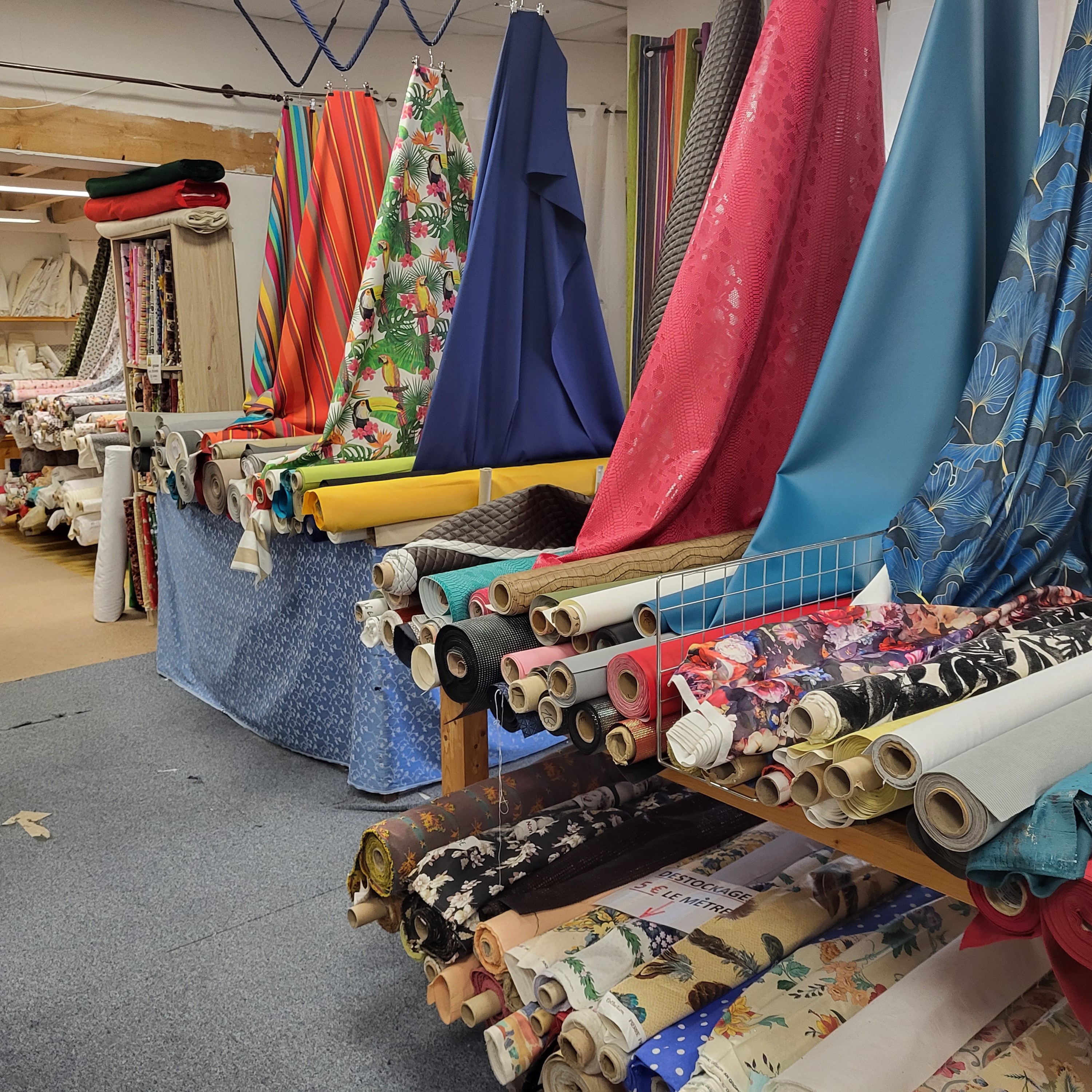 Un large assortiment de rouleaux de tissus colorés et à motifs exposés dans un magasin de tissus, avec différentes textures et designs visibles.