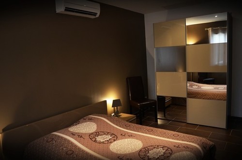 Une chambre à coucher moderne avec un lit douillet aux motifs beiges et bruns, une table de chevet éclairée, un fauteuil et une grande armoire à portes miroir.