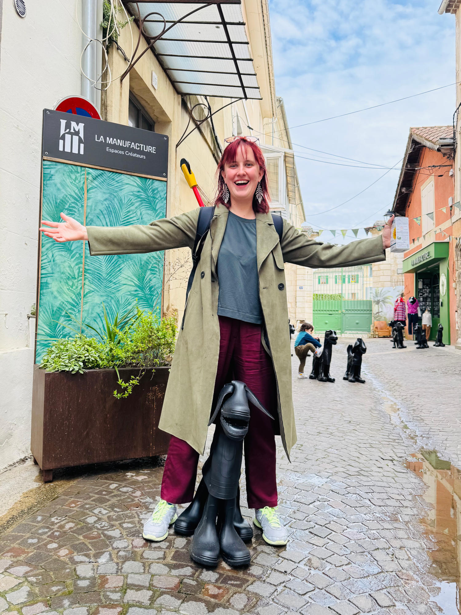 femme aux cheveux rouge accueillante devant une sculpture en forme de chien faite de bottes de pluie