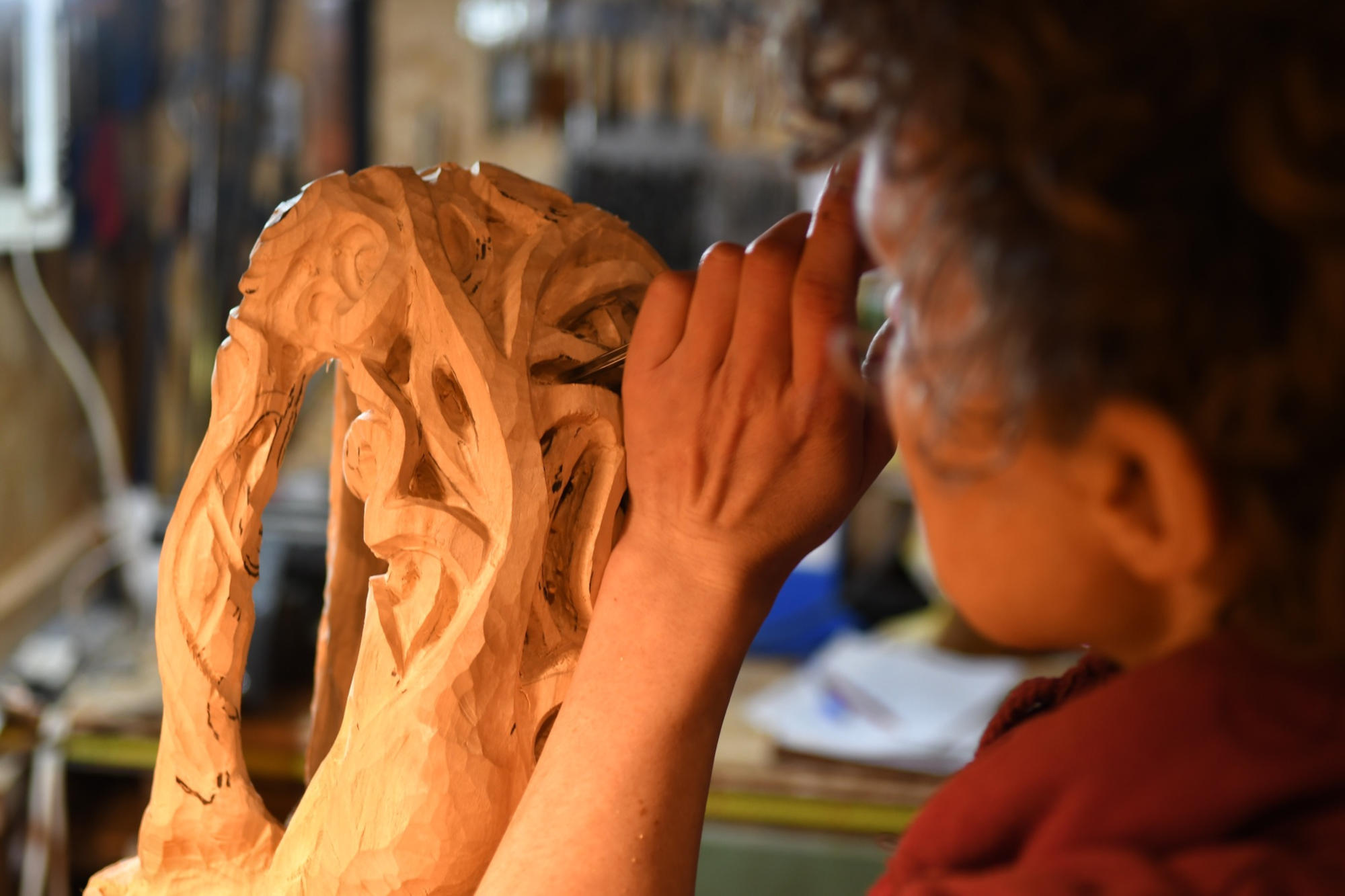 Une sculpteuse concentrée, travaillant sur une sculpture en bois détaillée avec des outils de gravure.