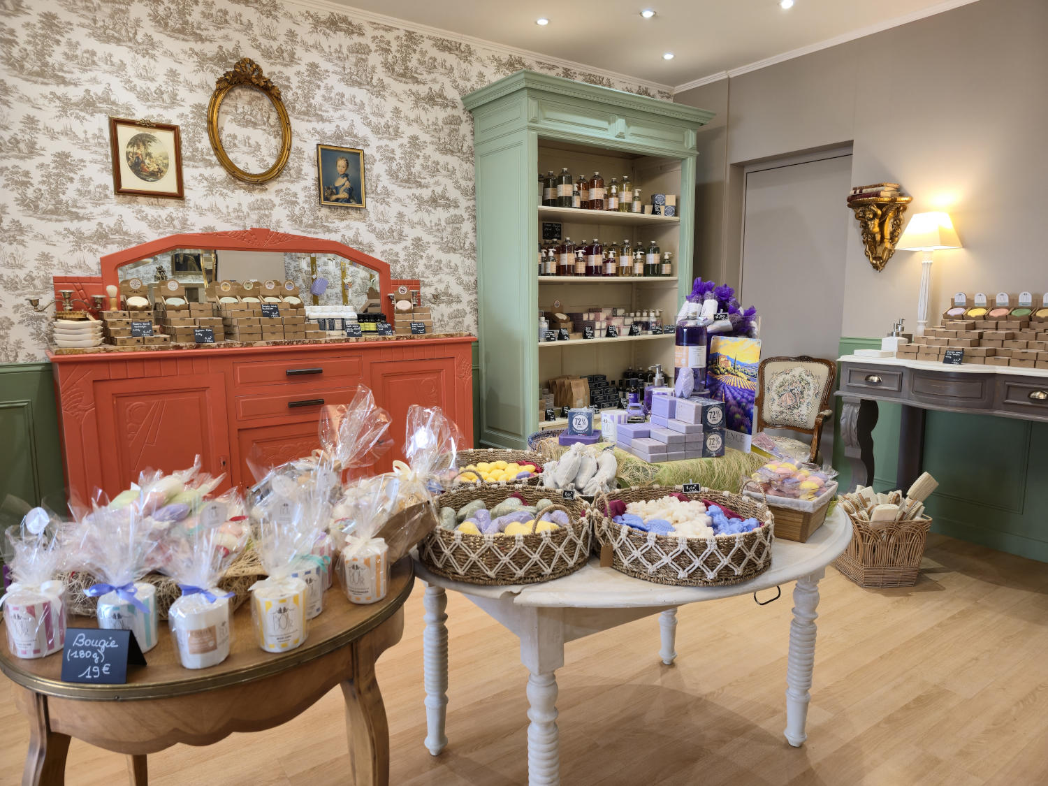 Intérieur d'une boutique vendant des produits artisanaux, avec des savons, bougies et cosmétiques sur des tables et étagères.