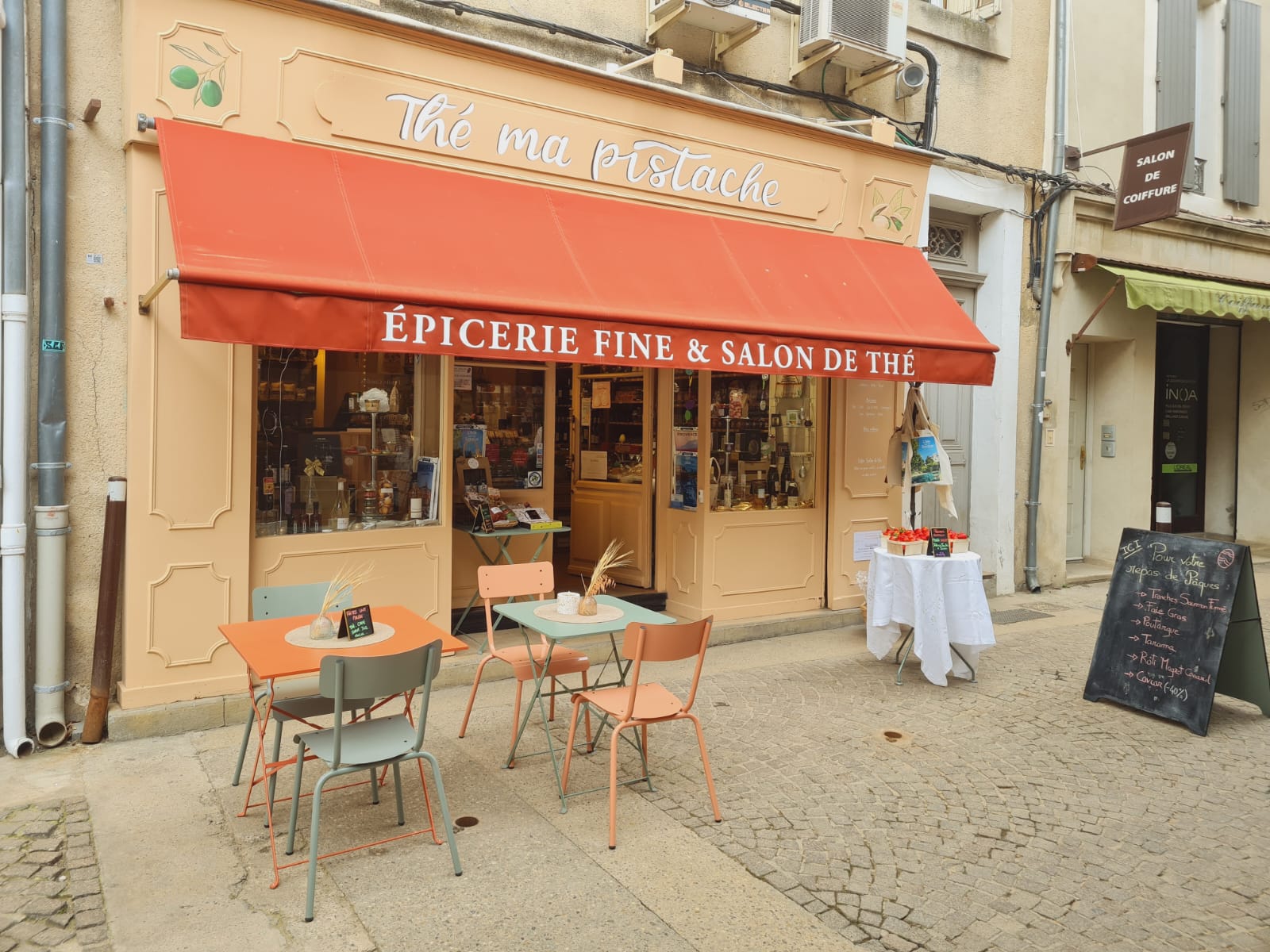 Devanture de l’épicerie fine et salon de thé Thé Ma Pistache, située rue de la République à L’Isle-sur-la-Sorgue, avec terrasse et tables installées devant la boutique.