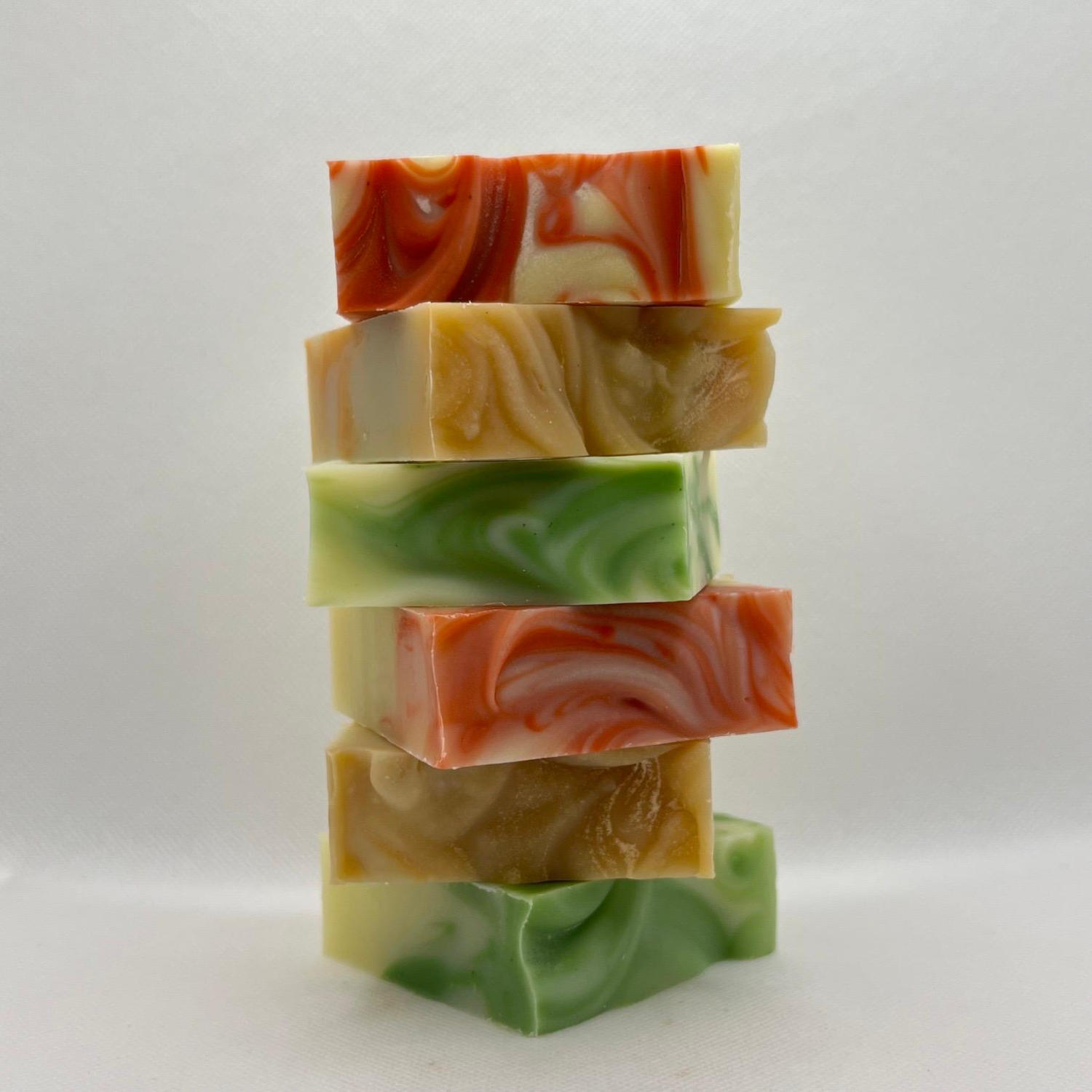 Une pile de six pains de savon artisanaux aux motifs de marbrure de couleurs variées, comme le rouge, le vert et le jaune.