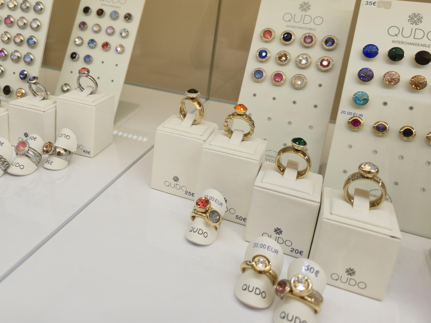 Une sélection de bagues et de pierres précieuses interchangeables de la marque Qudo, présentées dans une vitrine de magasin.