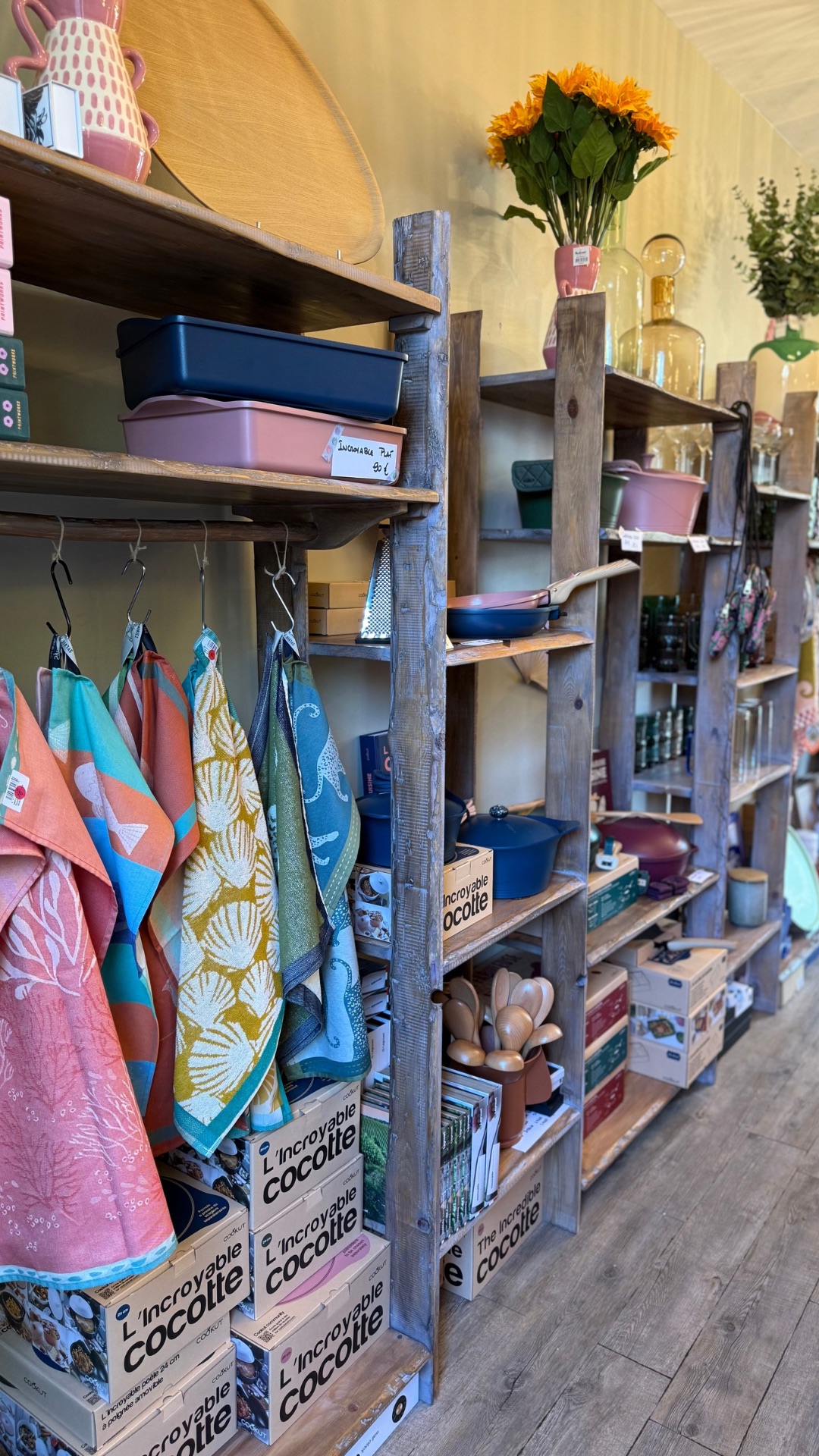 Présentoirs en bois grisé avec torchons colorés, poeles de couleur rose ou bleu, marmites e fonte de couleurs acidulées, verres, grands vases, bouquets de fleurs