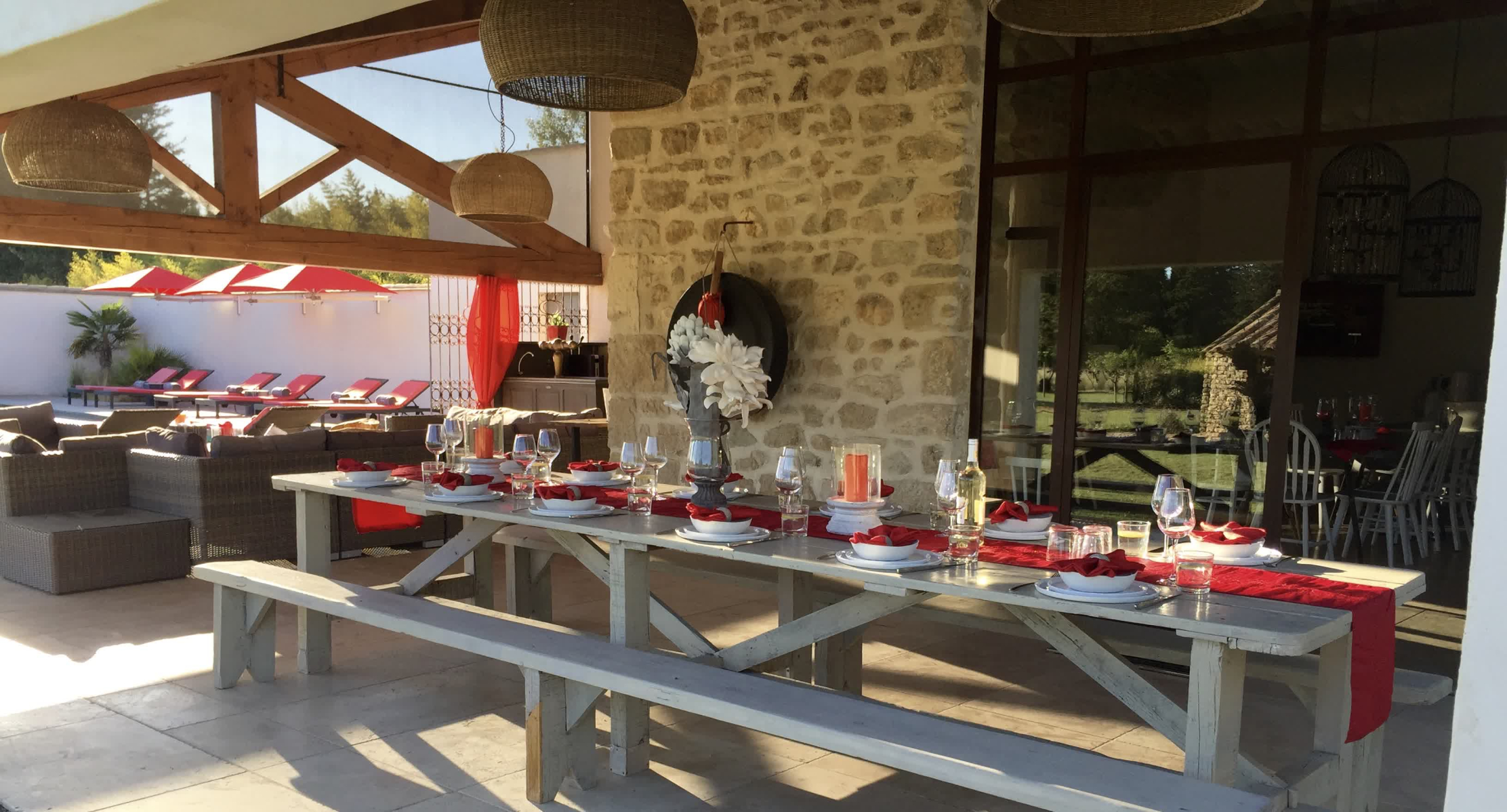 Grande terrasse conviviale avec table dressée sous pergola, espace lounge et vue sur la piscine et les transats, idéale pour les repas en plein air.