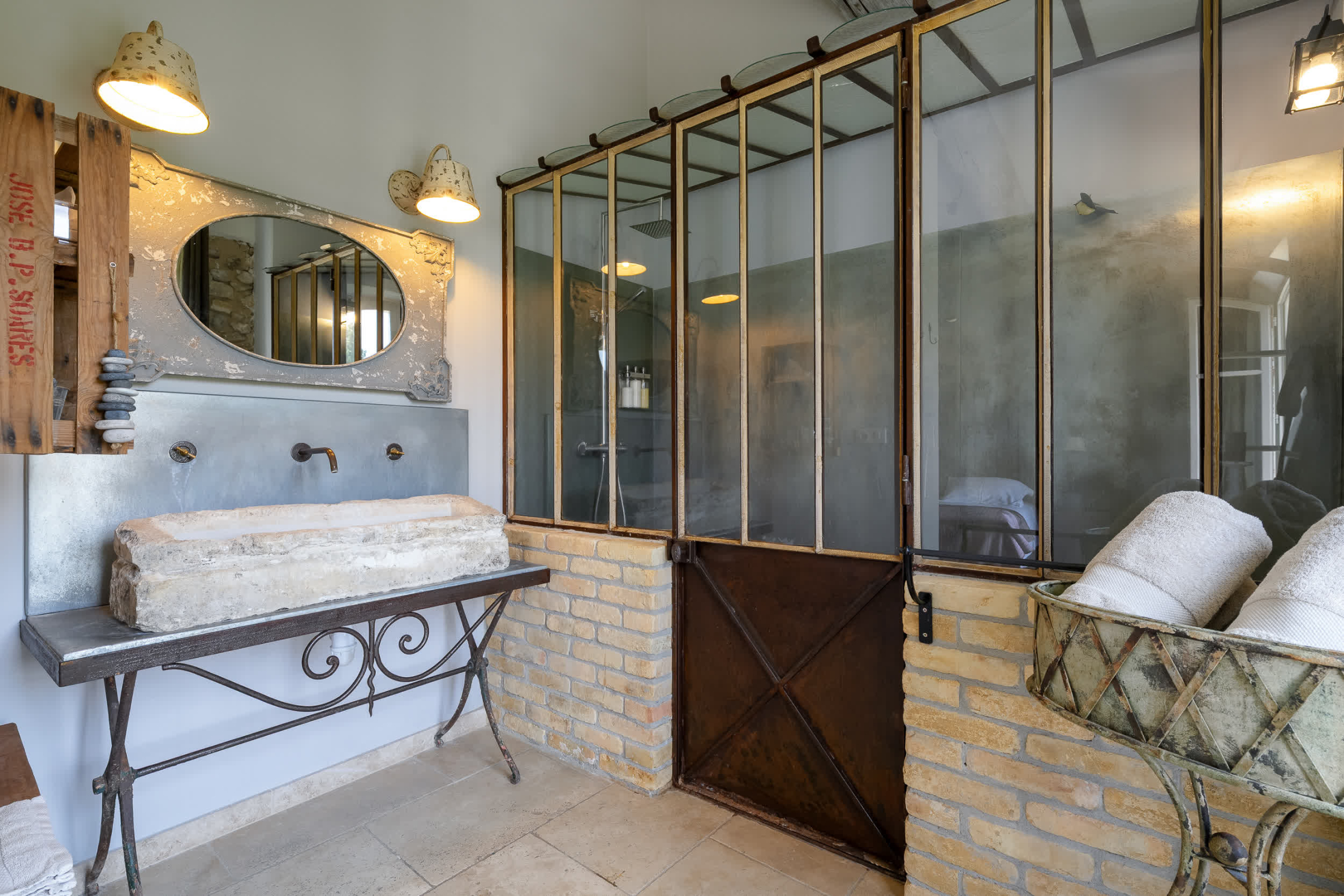Salle de bain au style industriel et authentique avec vasque en pierre, robinetterie murale et grande douche vitrée aux structures métalliques.