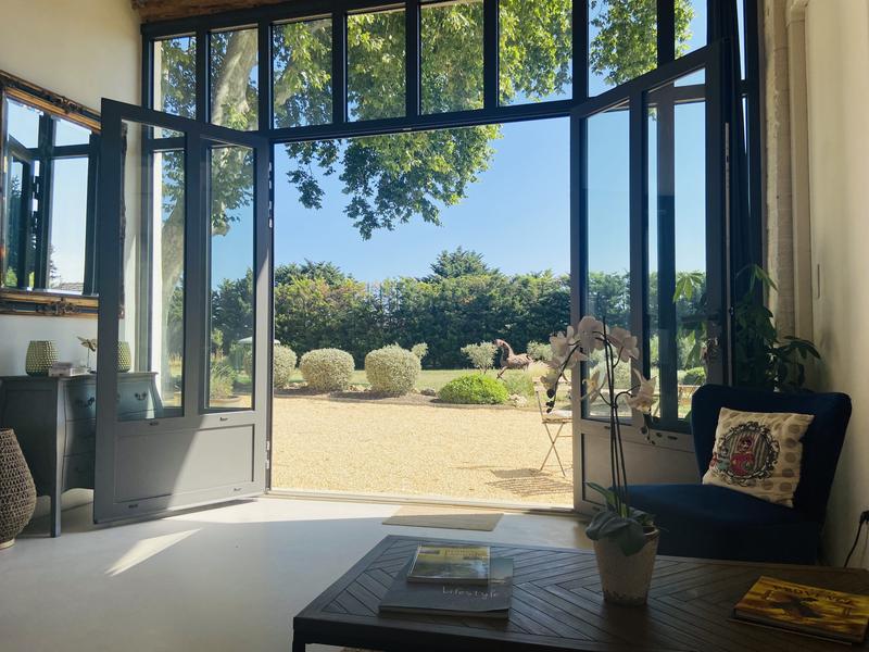 Salon lumineux ouvrant sur un jardin verdoyant sous un grand platane.