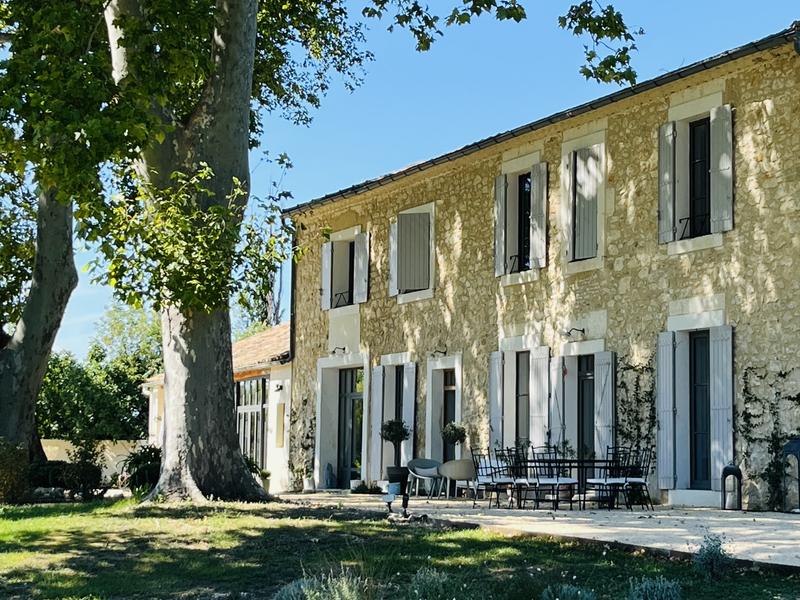 Maison provençale en pierre avec volets gris, terrasse ombragée et grand jardin.