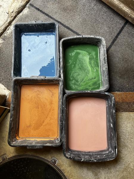 Bacs de pigments liquides bleu, vert, ocre et rose utilisés pour la fabrication artisanale des carreaux de ciment.