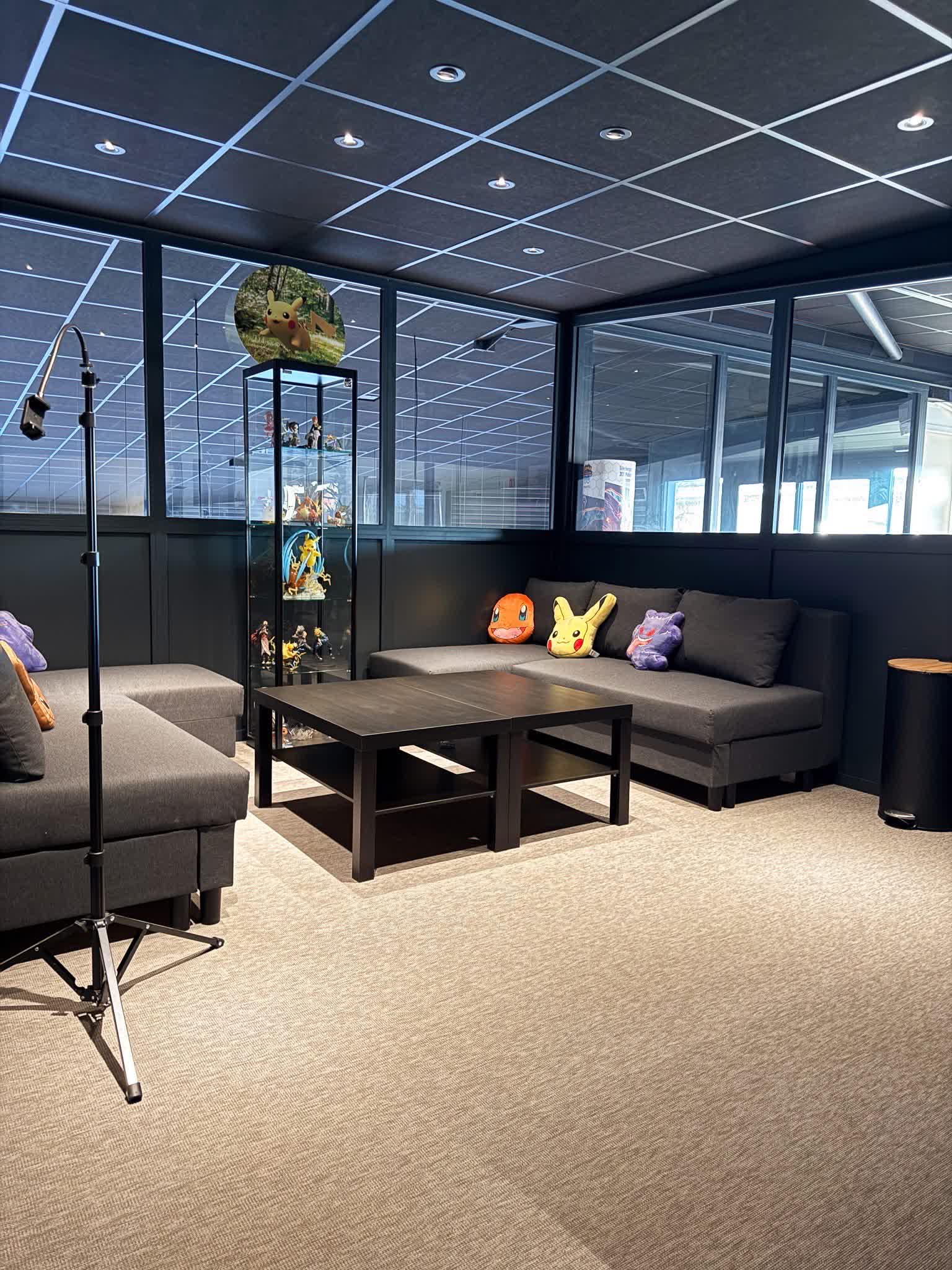 Un coin détente moderne et chaleureux, avec canapés confortables, figurines exposées et peluches colorées, idéal pour échanger entre passionnés.