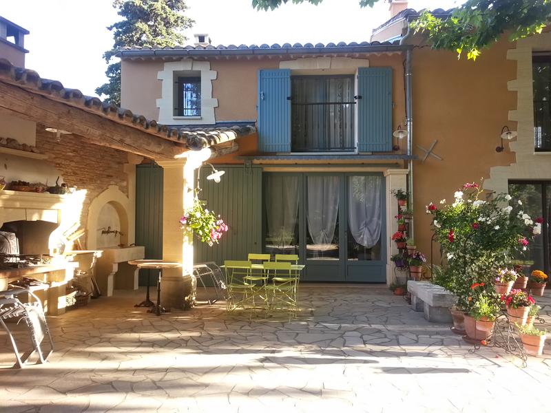Véranda extérieure verte avec chemin en pierre devant une grande batisse provençale et sa cuisiné d'été.