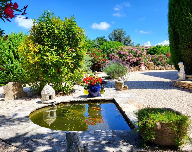 Un jardin méditerranéen avec des arbres, des arbustes, une statue, et une villa en