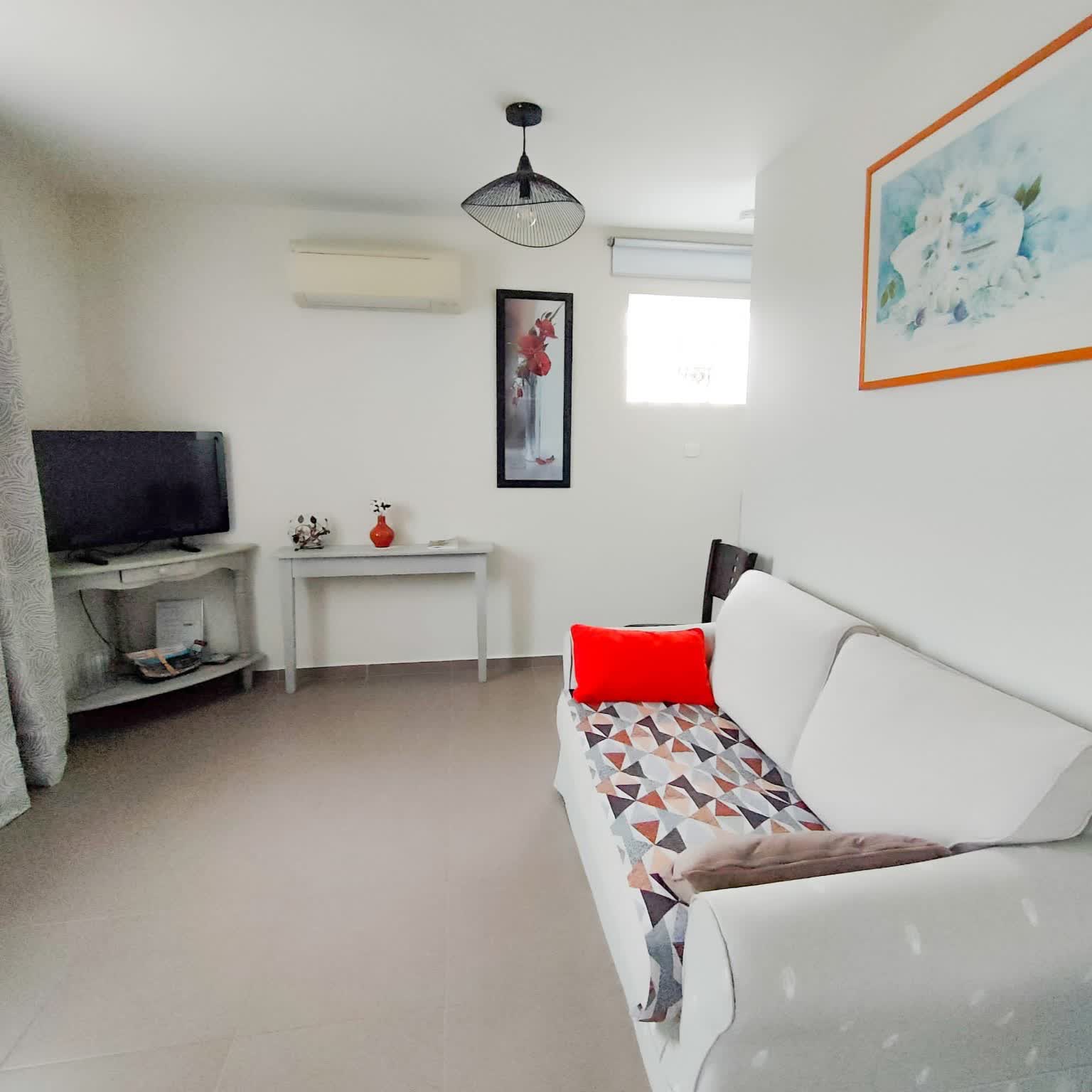 Salon blanc ambiance calme avec un canapé gris et télévison au fond
