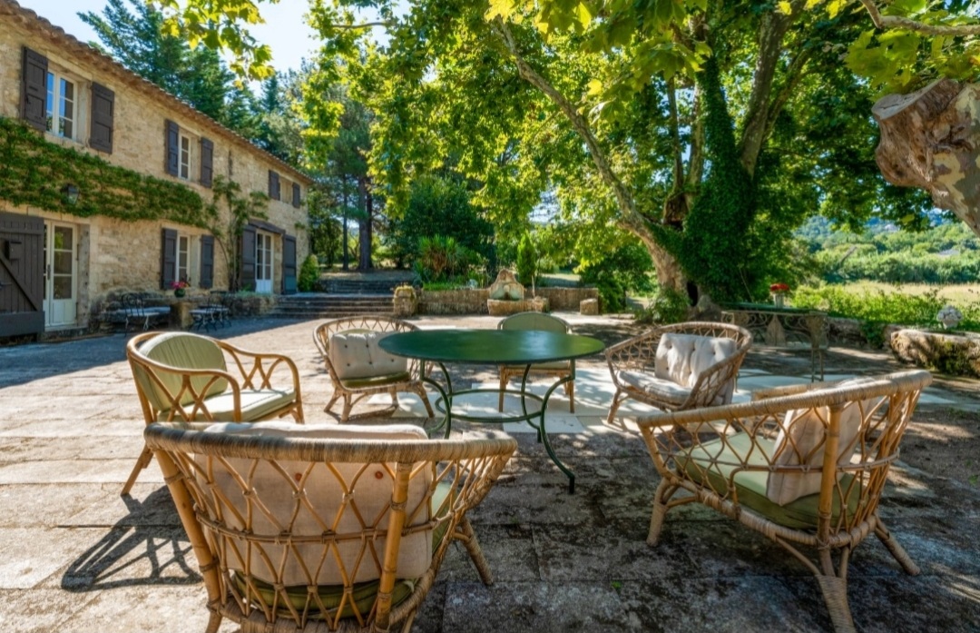 Salon de jardin en rotin exterieur à côté 'un mas provençal entouré d'abres