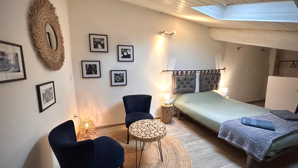 Chambre en mezzanine sous plafond mansardé, avec grand lit double et coin détente. Décoration douce et soignée, éclairage chaleureux et atmosphère cosy propice au repos.