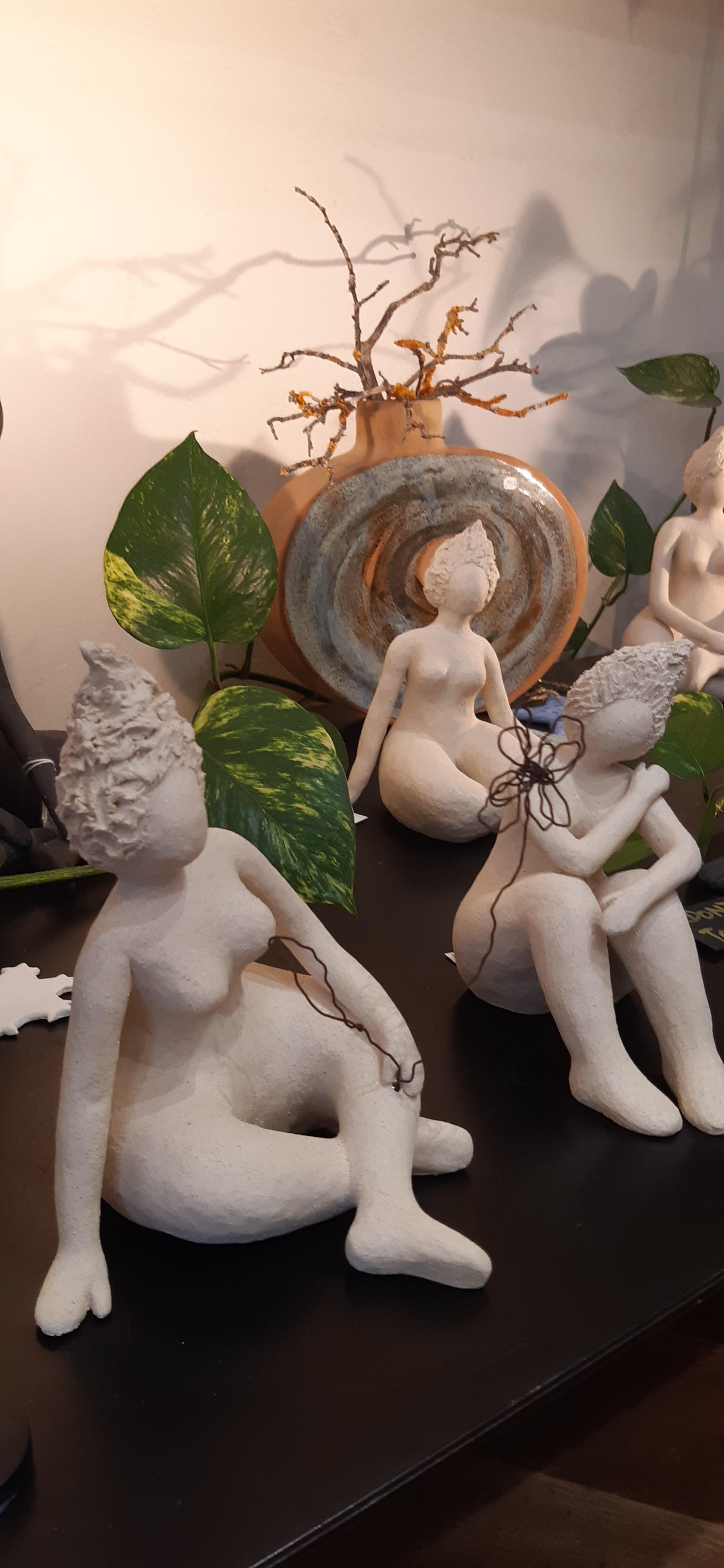 Petites sculptures en céramique claire représentant des silhouettes féminines assises, aux formes douces et épurées.