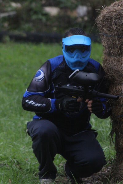 Paintball, homme en position accroupie derrière un ballot de paille. 