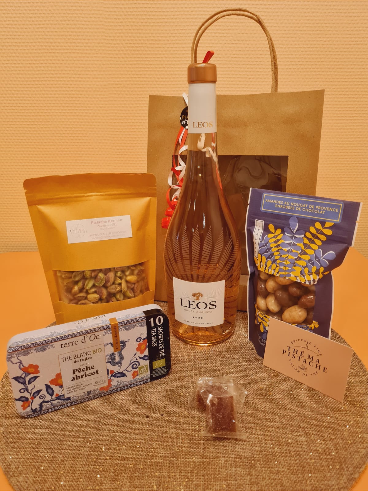 Sélection de produits gourmands et régionaux proposée par la boutique : pistaches, thé, amandes enrobées de chocolat et bouteille de vin du Domaine Léos, idéale pour un coffret cadeau.
