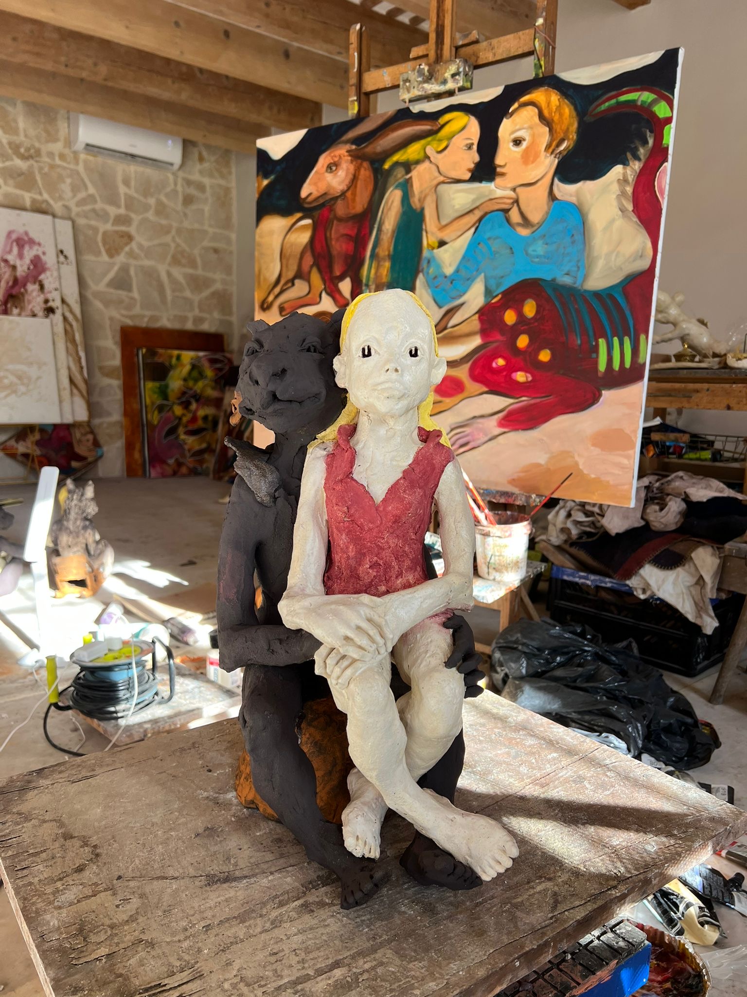 Peinture représentant des personnes et des animaux avec une sculpture d'un animal et d'une femme devant