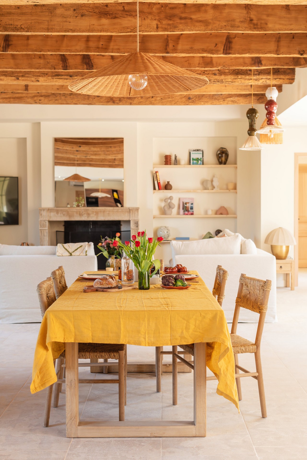 Une grande pièce de vie lumineuse à l’esprit provençal contemporain, mêlant poutres apparentes, mobilier en bois naturel et décoration chaleureuse. La table conviviale dressée au centre du salon invite à partager un moment de détente dans une atmosphère élégante et authentique.