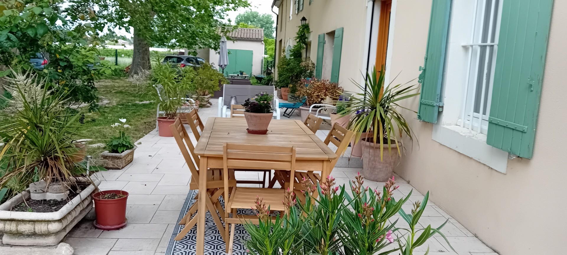 Une terrasse extérieure agréable avec table en bois, entourée de plantes, offrant un cadre calme et verdoyant.