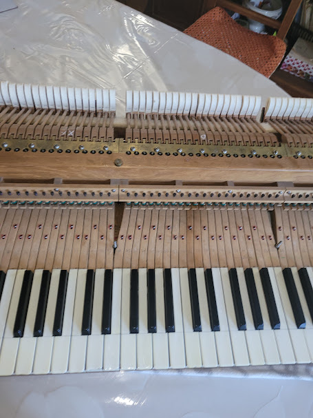 ### Photo 4 – Clavier et mécanique de piano en restauration  Vue détaillée d’un piano en cours de démontage et de restauration dans l’atelier de Lucas Gauthier-Lurty. Le clavier et la mécanique apparaissent partiellement déposés afin de permettre un travail précis de réglage, de nettoyage et de remise en état des éléments internes de l’instrument. Cette étape essentielle contribue à retrouver la qualité de toucher et la précision sonore du piano.