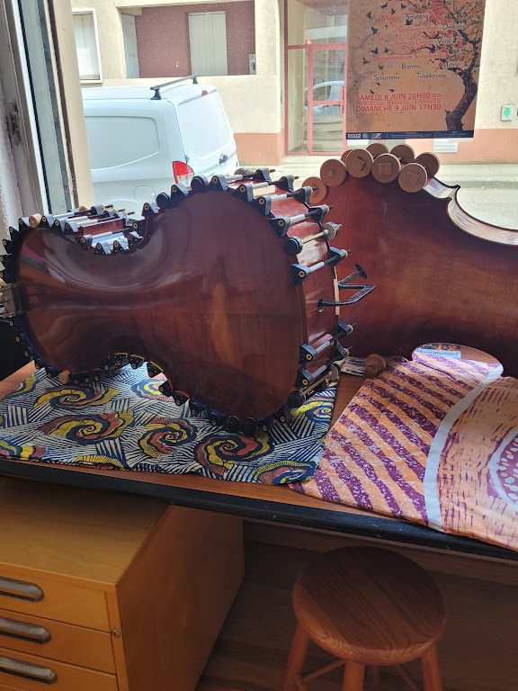 Vue d’une contrebasse démontée en cours de restauration dans l’atelier-boutique de L’Isle-sur-la-Sorgue. Les différentes pièces de l’instrument révèlent le travail de démontage, de réparation et de remise en état réalisé avec soin afin de préserver les qualités acoustiques et esthétiques de cet instrument à cordes.