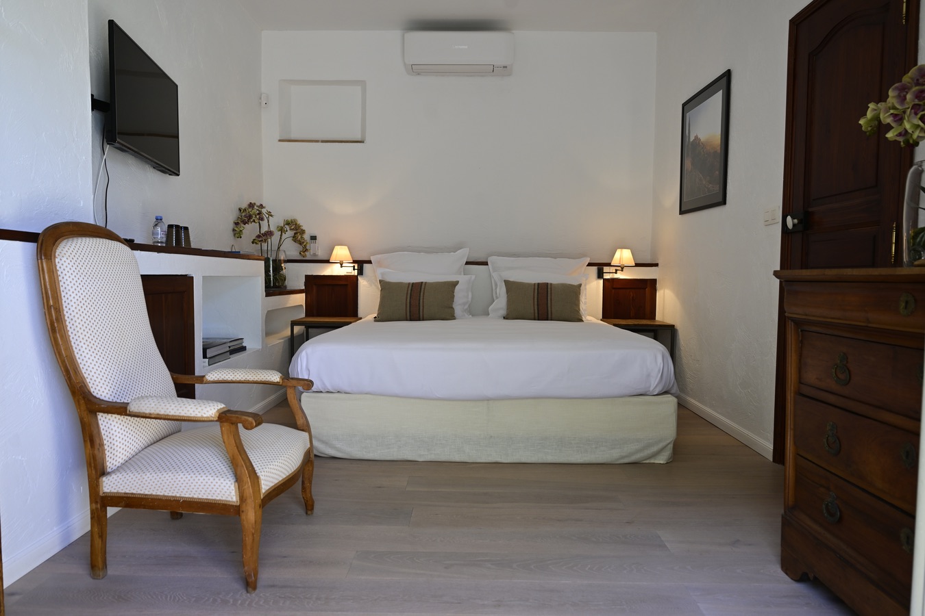 Cette chambre lumineuse allie sobriété et charme provençal avec son mobilier en bois ancien, ses tons naturels et sa décoration épurée. Le grand lit double, les éclairages chaleureux et les équipements modernes créent une ambiance confortable et apaisante, idéale pour un séjour au calme au cœur de la Provence.