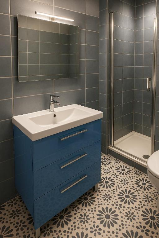Salle d’eau contemporaine avec douche, meuble vasque bleu et carrelage graphique au sol. Un espace rénové alliant confort moderne et détails décoratifs soignés.