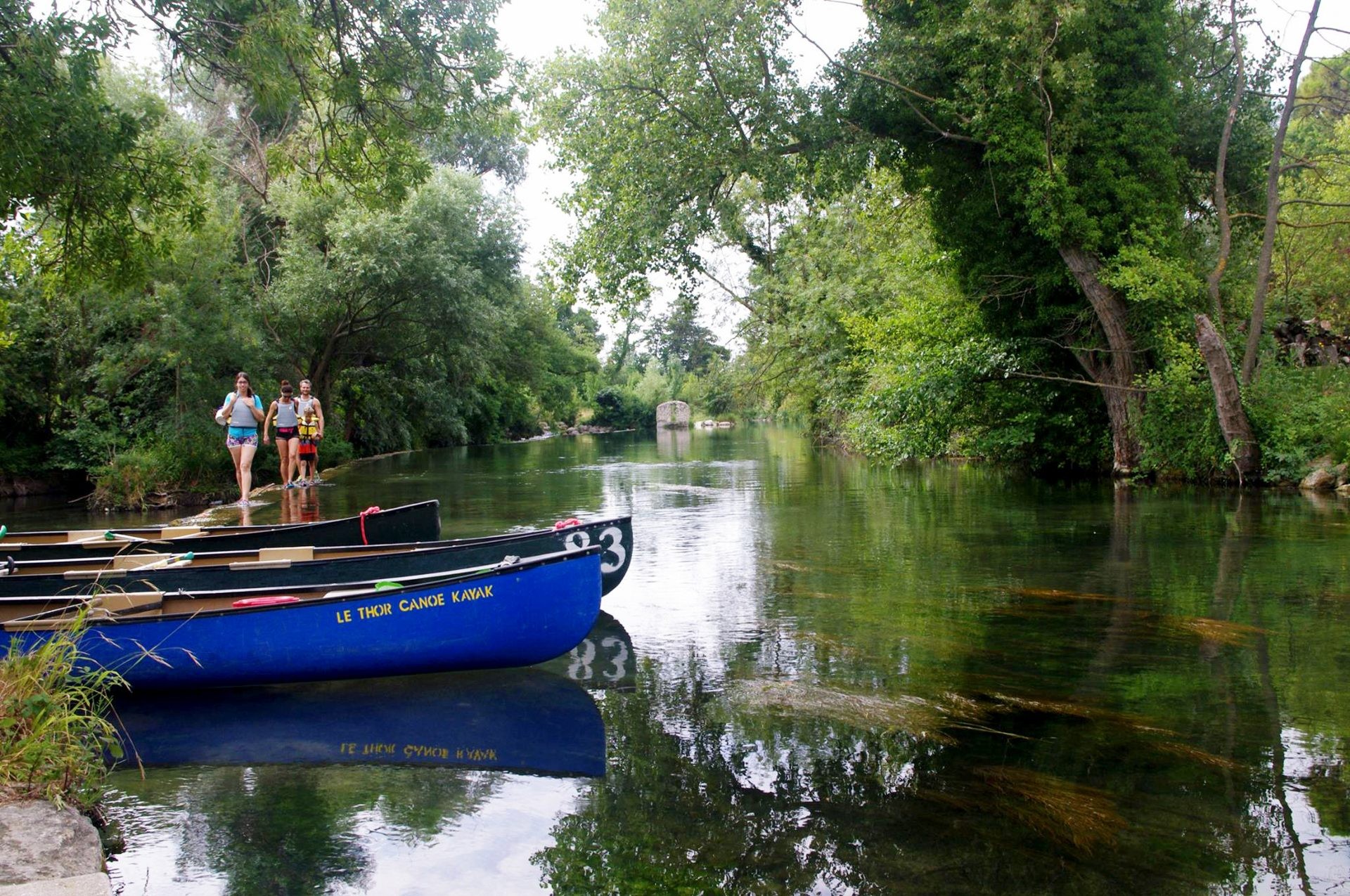 Canoës du Club de canoë-kayak du Thor amarrés sur les eaux cristallines de la Sorgue, dans un environnement calme et verdoyant propice à la détente et aux loisirs nature.