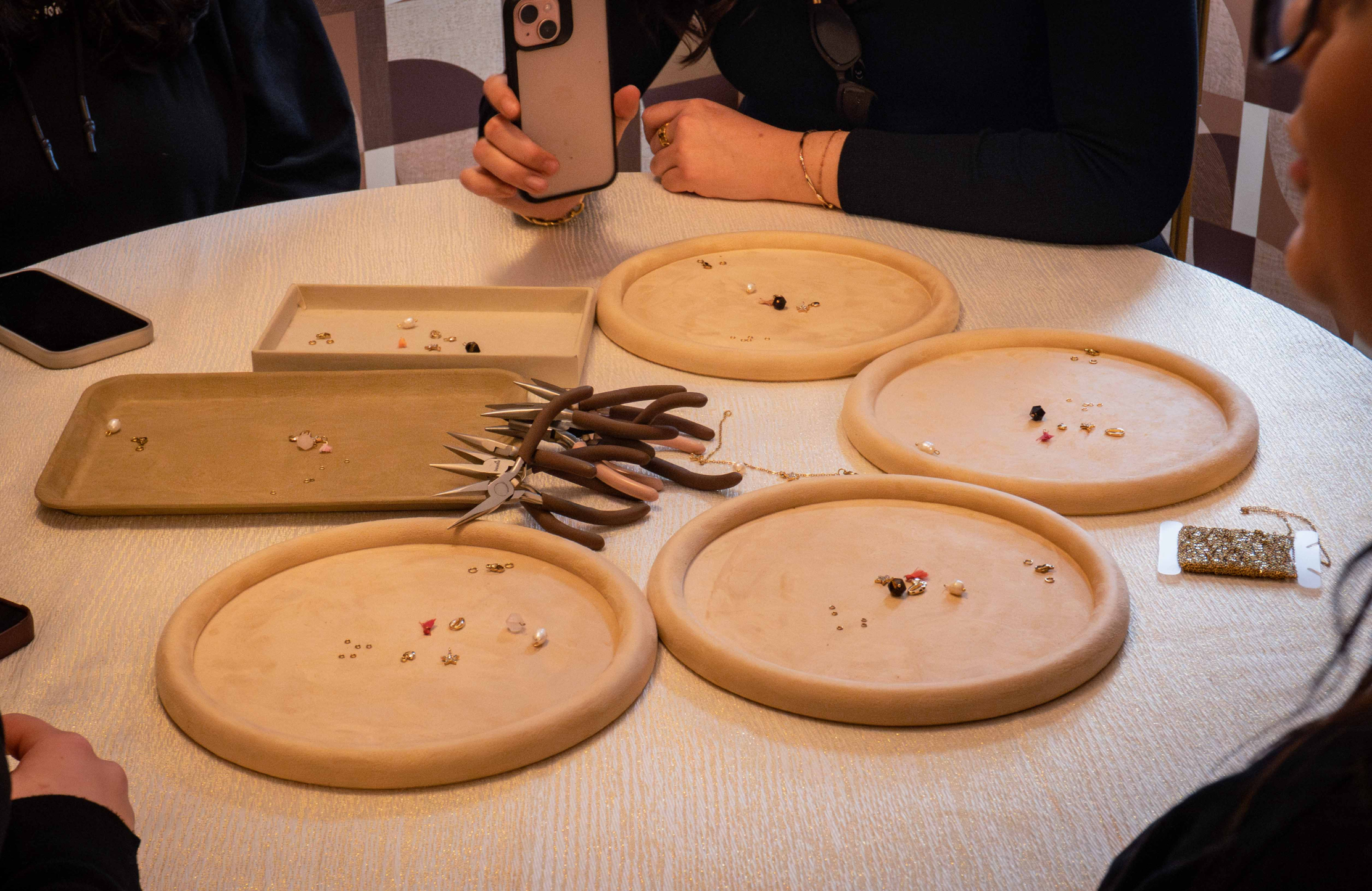 Une table d’atelier est préparée avec des plateaux, des perles et des outils de bijouterie. Les participantes réalisent leurs créations dans une ambiance calme et créative.