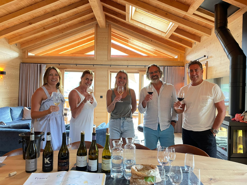 Un groupe de cinq participants prend part à un atelier de dégustation de vins dans un chalet lumineux. Verres à la main, ils découvrent différentes cuvées dans une ambiance conviviale et chaleureuse, guidés par une approche pédagogique et sensorielle du vin.