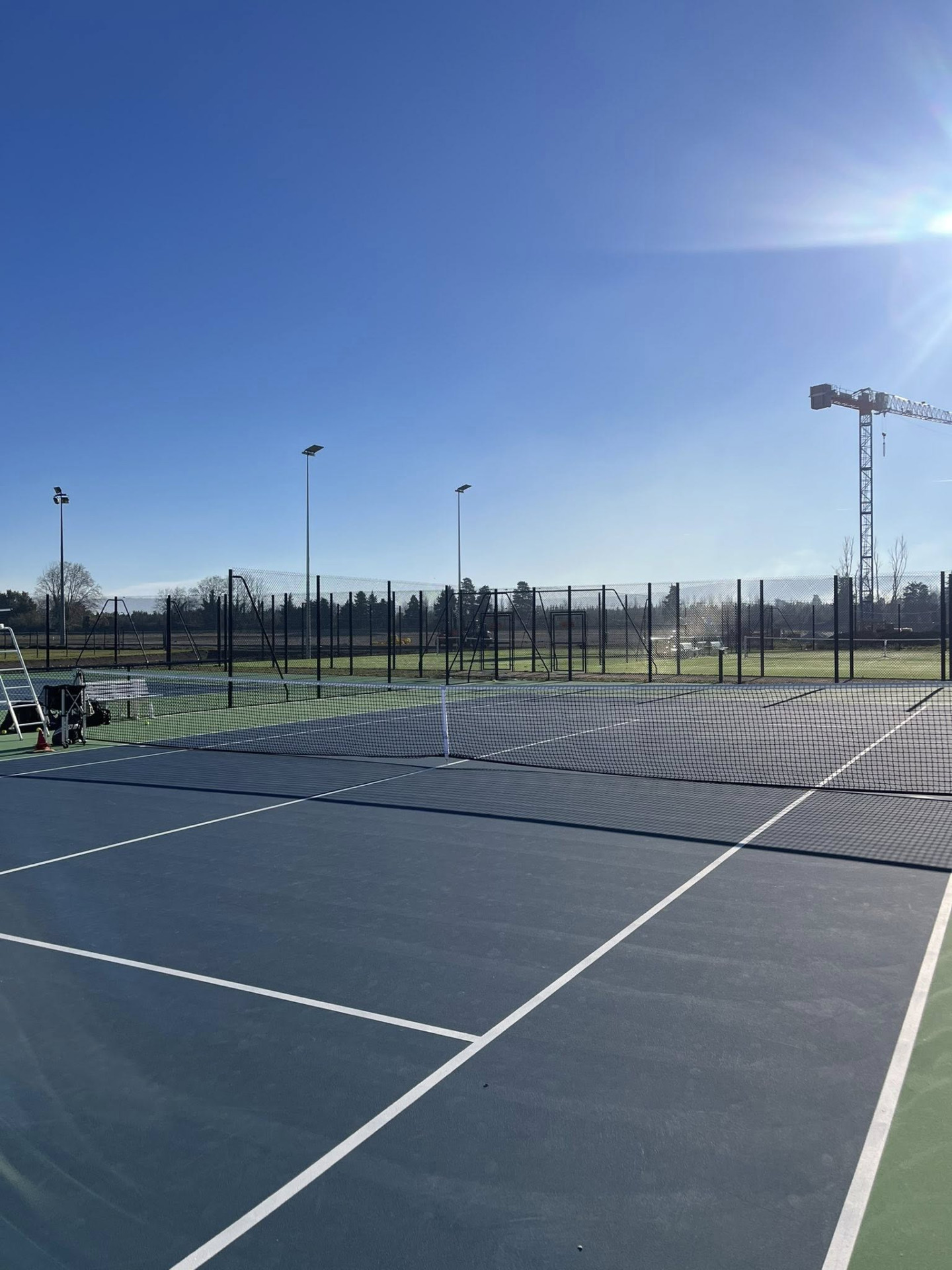 **Description :** Vue d'ensemble des courts de tennis extérieurs du complexe sportif. Les terrains, entièrement rénovés, offrent un espace de jeu moderne et sécurisé, idéal pour la pratique du tennis en loisir comme en compétition, dans un environnement dégagé et ensoleillé.