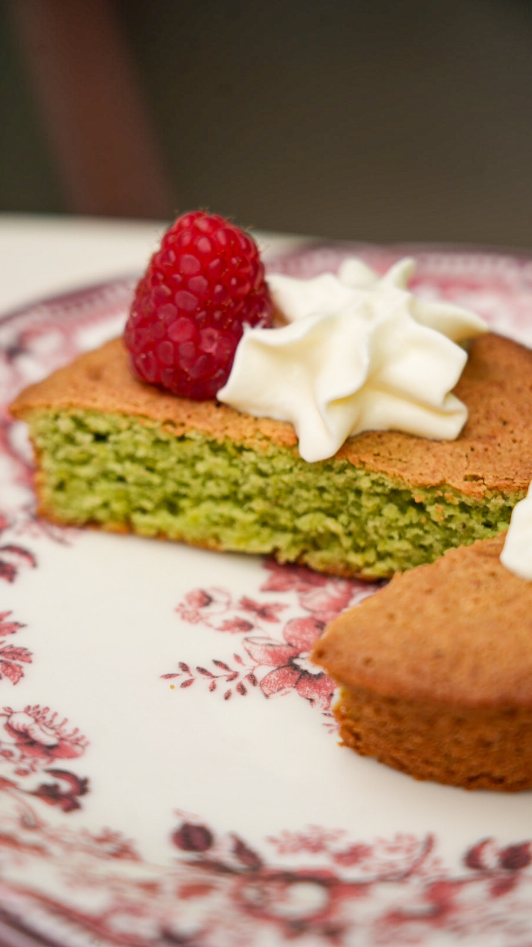 Une part de gâteau moelleux au thé matcha dévoile une mie tendre d'un vert délicat. Dressée dans une assiette au décor vintage, elle est agrémentée de rosaces de crème fouettée et d'une framboise fraîche qui apporte une touche de couleur et de fraîcheur. Une présentation soignée qui met en valeur une pâtisserie aussi raffinée que gourmande, idéale pour accompagner une pause café ou un thé.