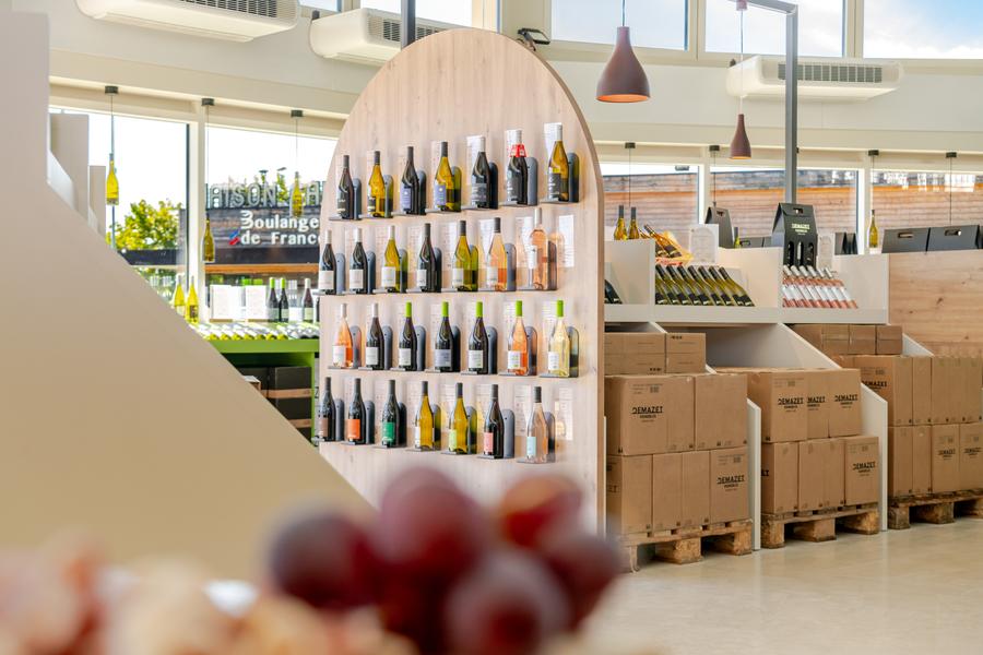 Vue intérieure du caveau Demazet, lumineux et contemporain, avec une large sélection de bouteilles de vin présentées sur des étagères en bois. L’espace met en valeur les différentes cuvées de la cave dans une ambiance moderne et accueillante.