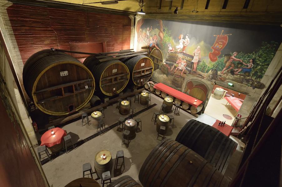 La salle des foudres Vue plongeante sur une salle de caractère aménagée au milieu d’imposants foudres et tonneaux en bois. Tables hautes et assises sont installées dans cet ancien espace de cave, décoré d’une grande fresque évoquant l’univers de la vigne et des vendanges.