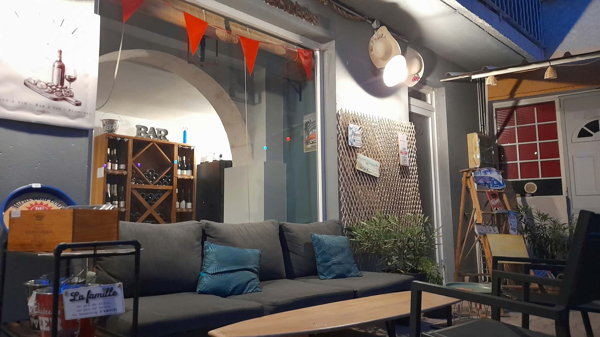 Un espace cosy et accueillant au sein de L’Isle Divine, aménagé avec un grand canapé, des fauteuils et une table basse. À l’arrière-plan, les bouteilles de vin rappellent l’identité de cave et bar à vin du lieu. La décoration chaleureuse et décontractée invite à s’installer confortablement pour partager un verre dans une ambiance conviviale à L’Isle-sur-la-Sorgue.