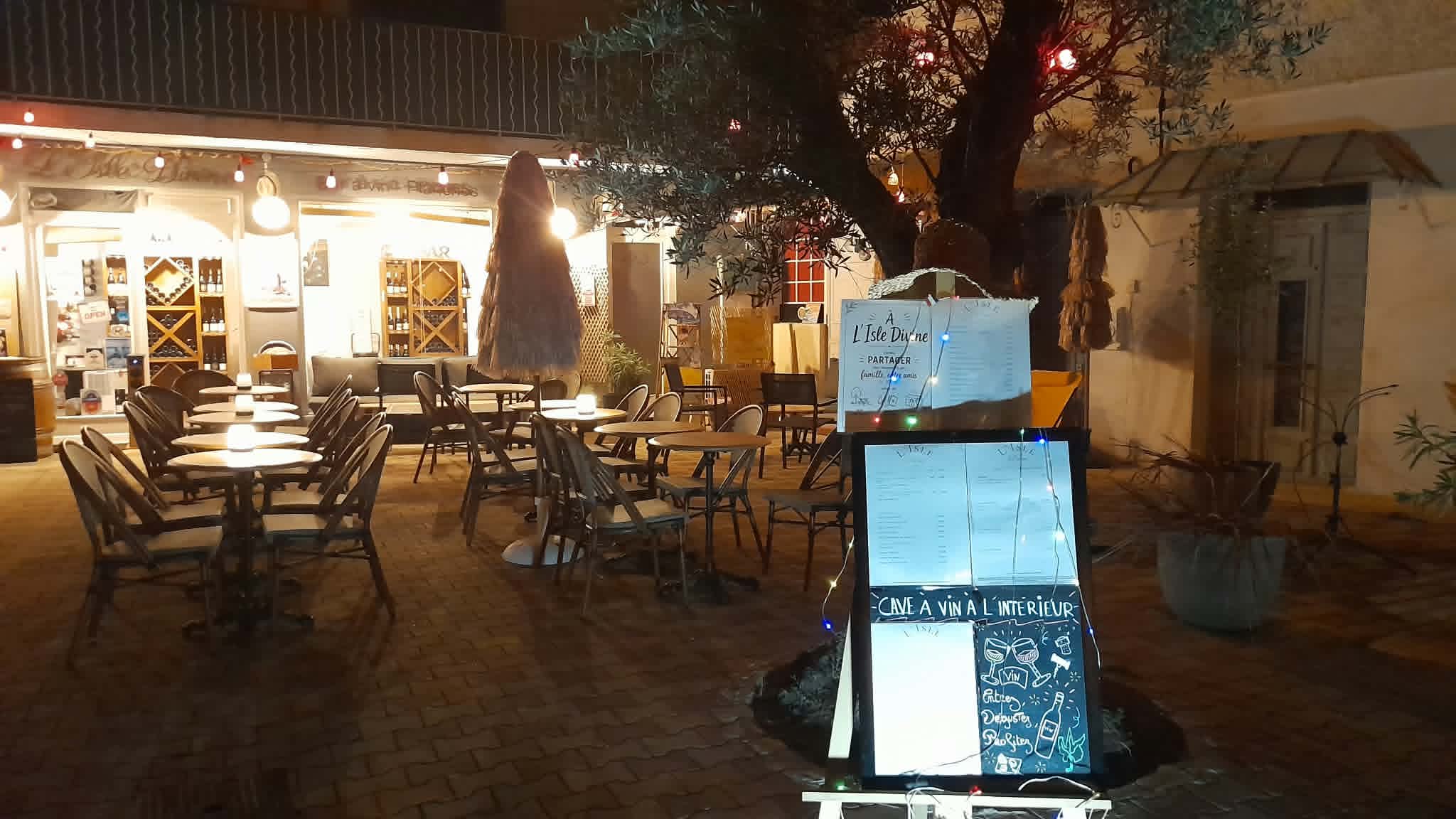 Terrasse de L’Isle Divine, cave et bar à vin à L’Isle-sur-la-Sorgue, aménagée autour d’un olivier et éclairée en soirée.