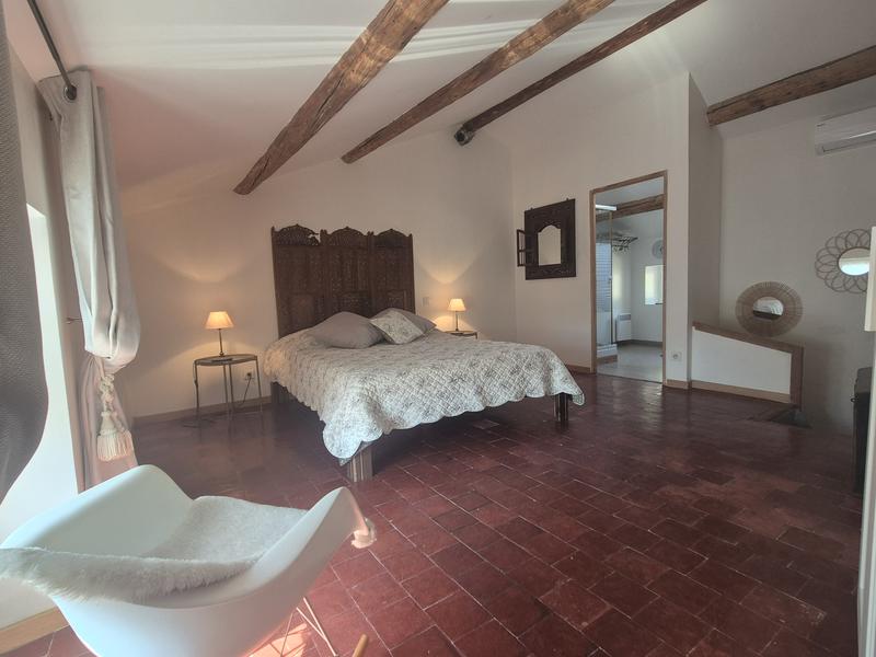Grande chambre lumineuse avec lit double, poutres apparentes et sol en tomettes anciennes. La pièce dispose d’un espace généreux, d’une décoration sobre et élégante ainsi que de la climatisation.