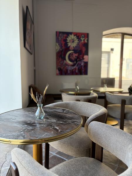 Vue intérieure d’Orlie à L’Isle-sur-la-Sorgue, avec des tables rondes effet marbre, des fauteuils aux tons beige et plusieurs œuvres colorées exposées aux murs. L’ensemble crée une atmosphère élégante, chaleureuse et contemporaine.