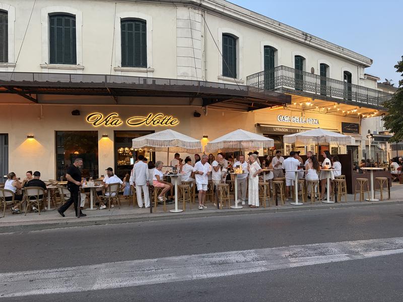 Façade et terrasse de Via Notte à L’Isle-sur-la-Sorgue, avec tables et espace bar installés le long de l’Esplanade Robert Vasse.