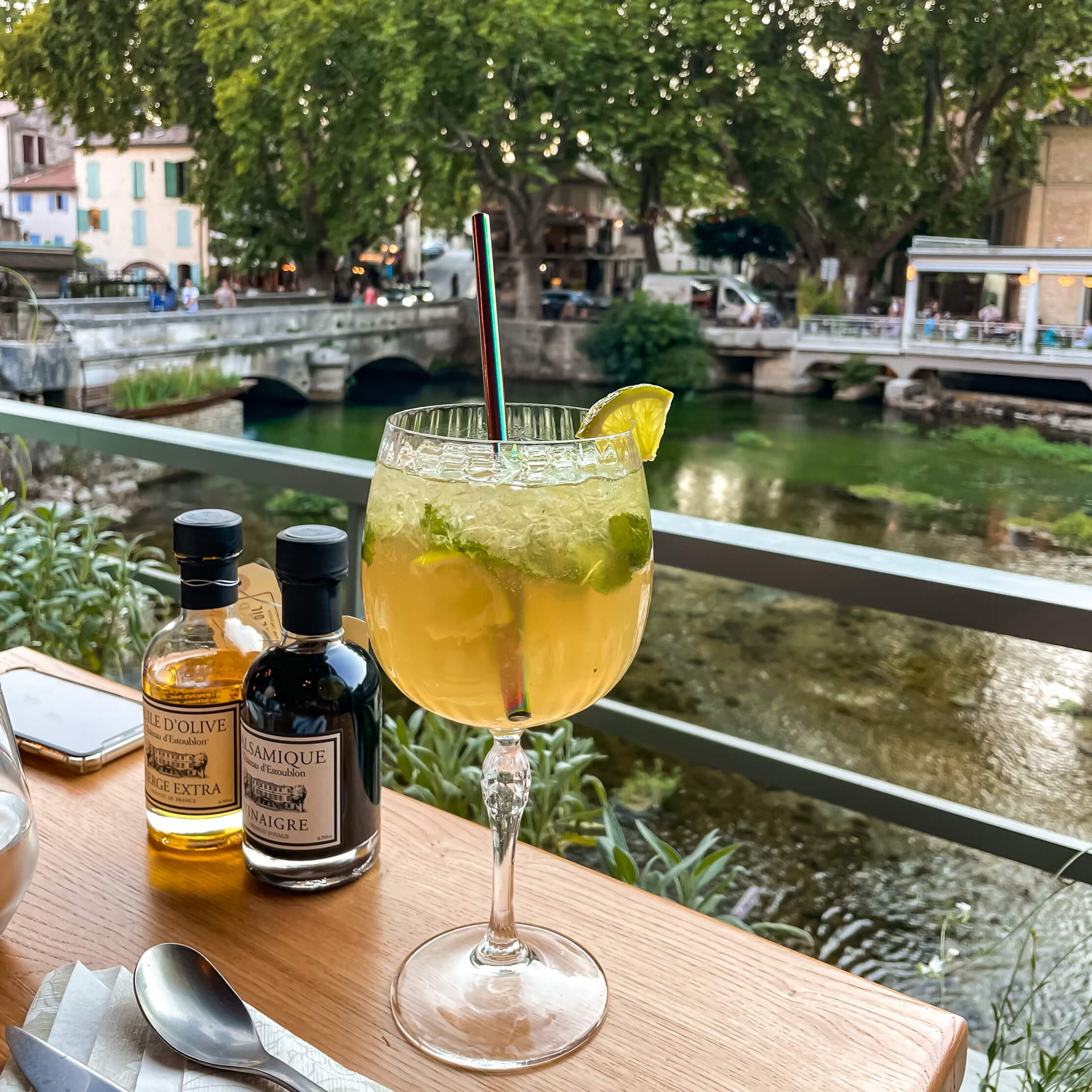 un verre de mojito est placé sur une table en bois avec vue sur la Sorgue