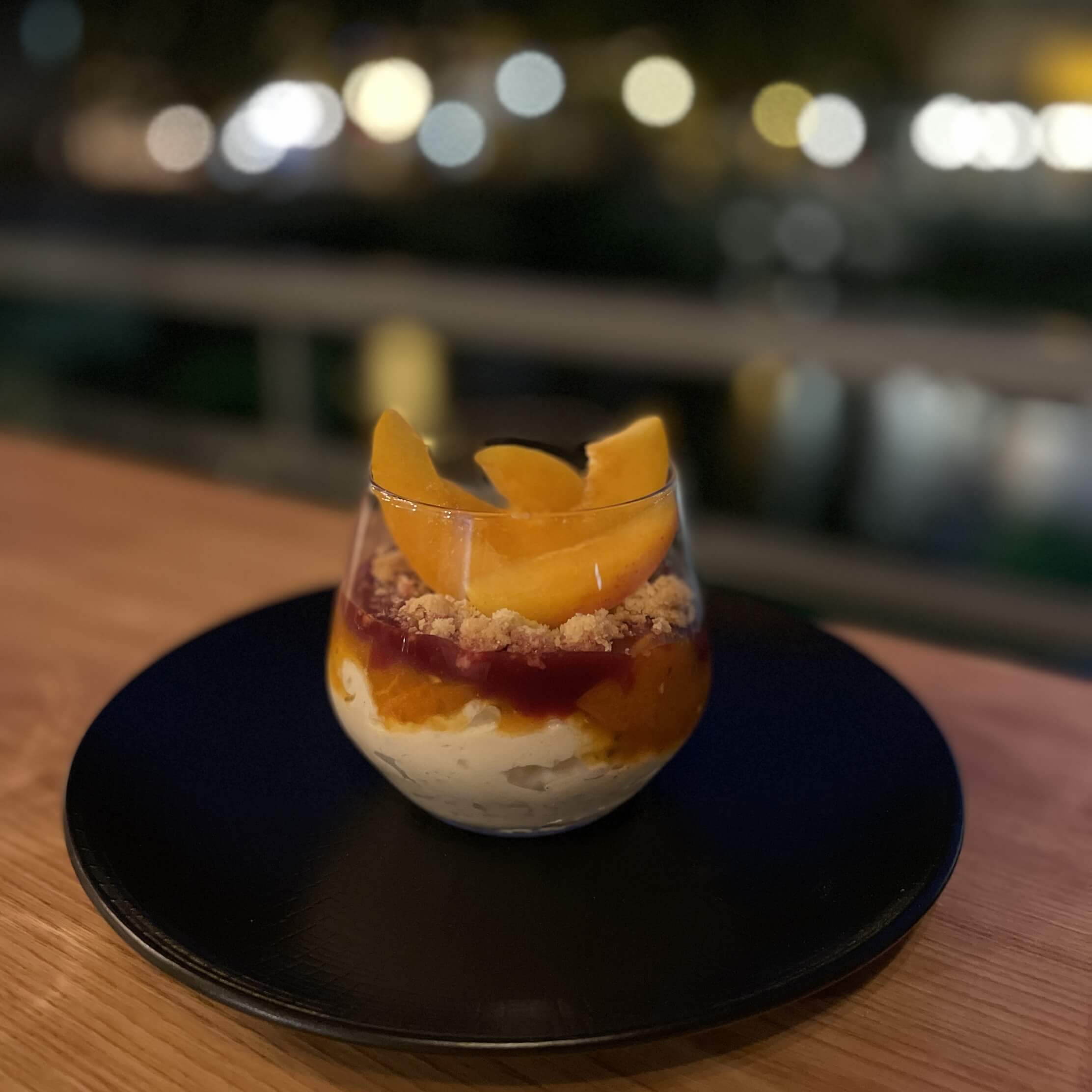 dessert crémeux surmonté de coulis de fruits jaunes et rouges, clairsemé de crumble et de tranches de fruits frais