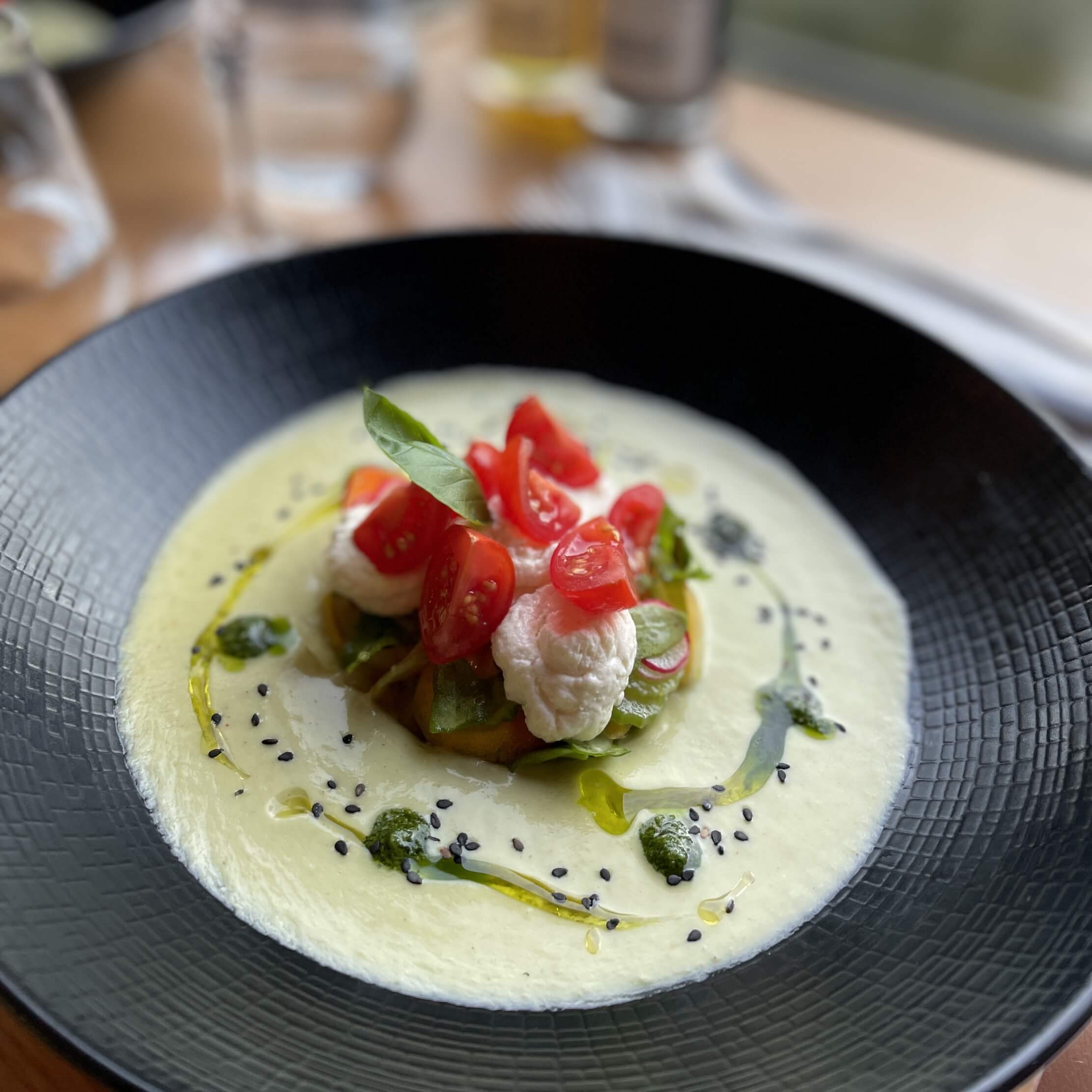 une assiette creuse noire dans laquelle est placée une entrée à base légumes baignant dans une sauce crémeuse